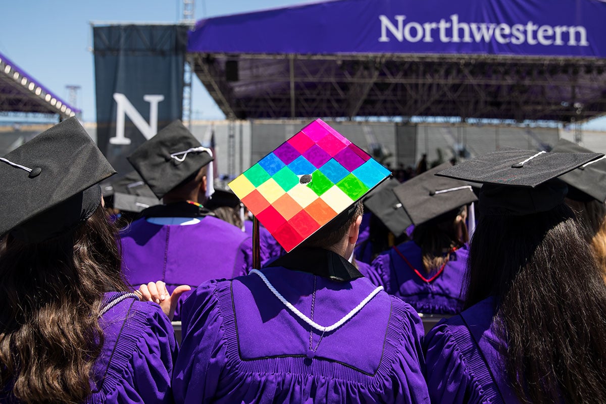 Student wearing rainbow colored academic cap during graduation ceremony